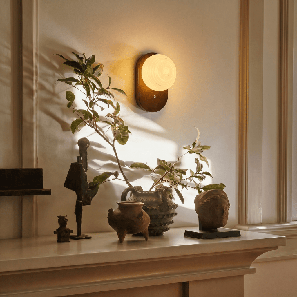 Clérachic wall lamp glowing above a mantel styled with small sculptures and a leafy branch.