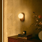 Clérachic wall lamp glowing above a dresser styled with a candle, a flower arrangement and a stack of books.