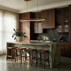 A Clérachic wood-grain bar pendant lights a marbled green kitchen island lined with woven leather counter stools.