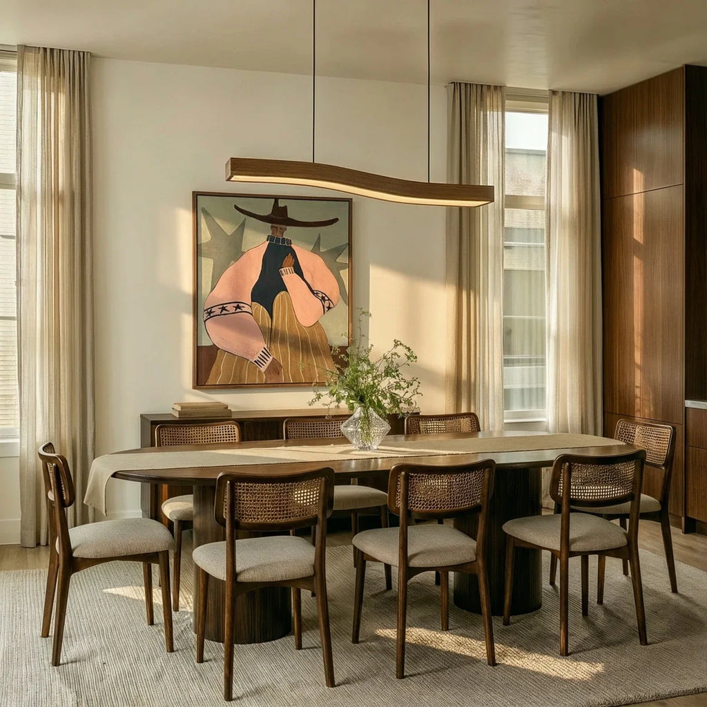 A Clérachic wood-grain bar pendant hangs above a long dining table set beneath a large framed painting.