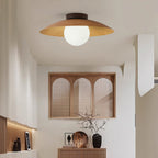 A Clérachic ceiling light in a natural wood-grain finish, with a pale glass globe, above a room with an arched rattan window and a sideboard.