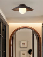 Lit softly, a Clérachic ceiling light with a dark wood-grain shade sits above an arched wooden doorway and a warmly lit hall.