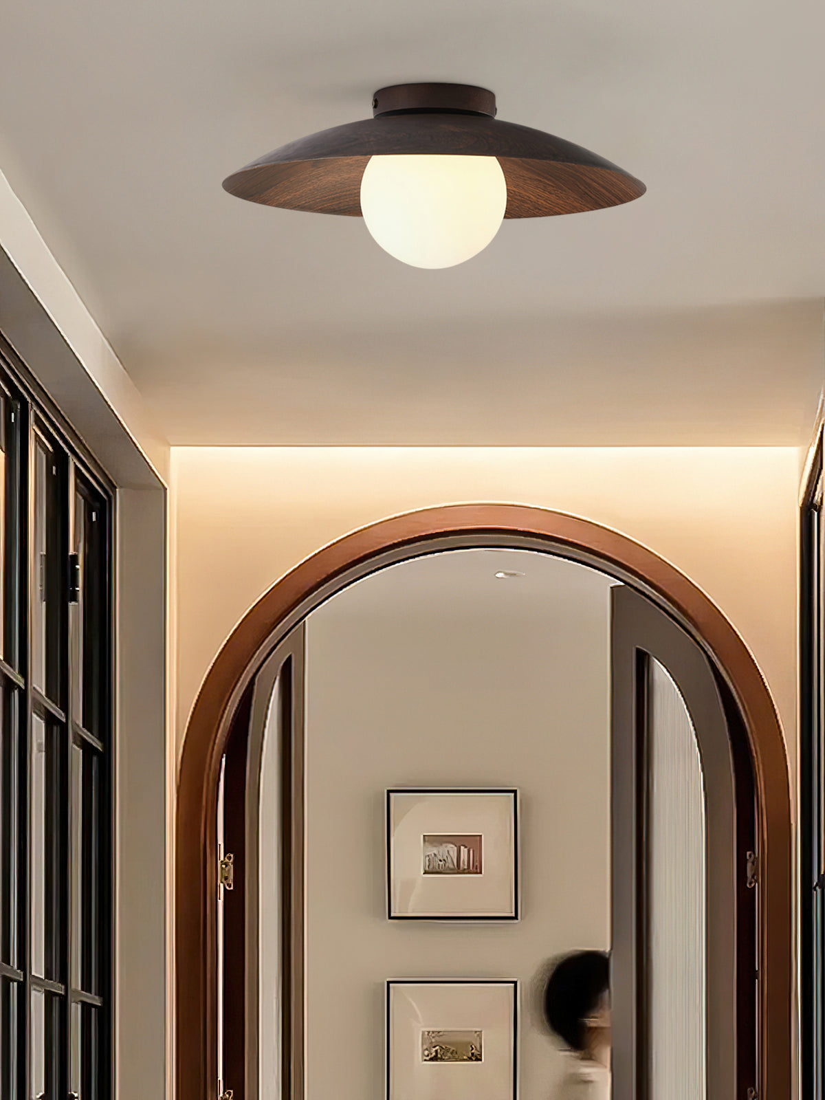 Lit softly, a Clérachic ceiling light with a dark wood-grain shade sits above an arched wooden doorway and a warmly lit hall.