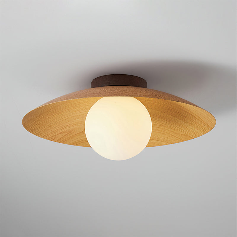 A Clérachic ceiling light in a natural wood-grain finish, lit warmly, with the frosted globe glowing under a wide shade.