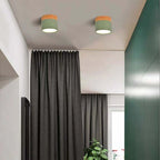 A pair of green Clérachic Wood-Grain Cylinder Ceiling Lights lit on a white ceiling above a curtained hallway.