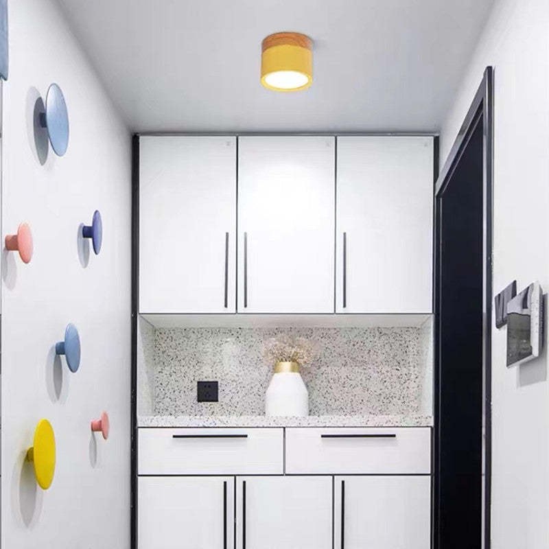 A yellow Clérachic Wood-Grain Cylinder Ceiling Light throwing a cone of light down a narrow entry over white cabinets.