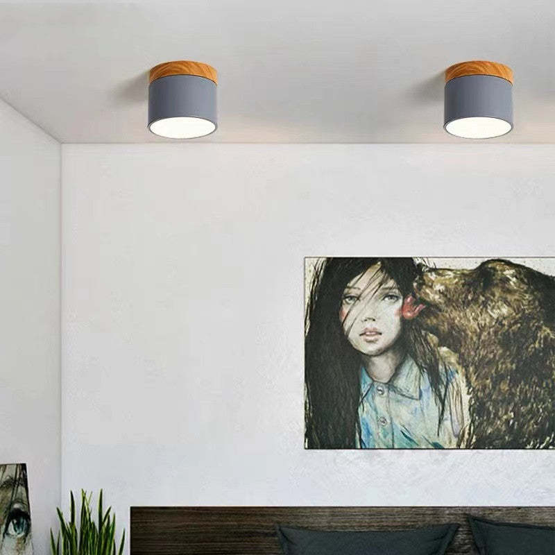 Two grey Clérachic Wood-Grain Cylinder Ceiling Lights lit above a bed, the wood-grain collar facing the room.