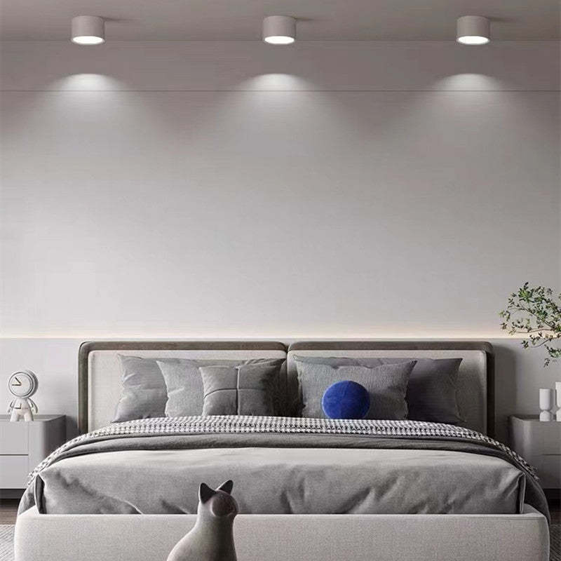 Three white Clérachic Wood-Grain Cylinder Ceiling Lights spaced above a grey upholstered bed, each throwing a tight cone.