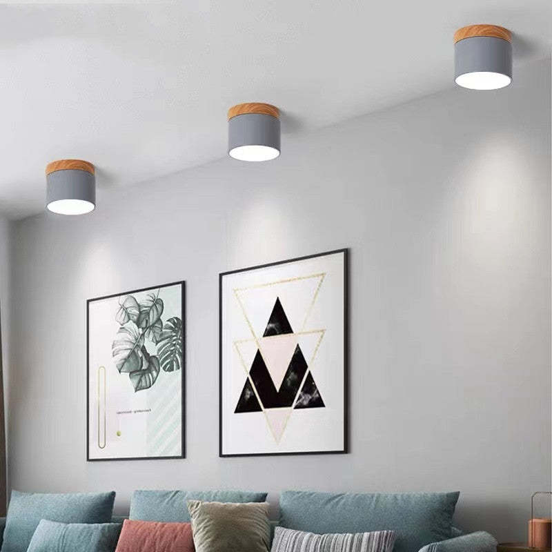 Three grey Clérachic Wood-Grain Cylinder Ceiling Lights stepping along a white ceiling above a sofa and framed prints.