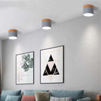 Three grey Clérachic Wood-Grain Cylinder Ceiling Lights stepping along a white ceiling above a sofa and framed prints.
