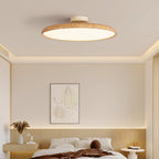 A light wood-grain Clérachic ceiling light lit warm over a bedroom with a pale wood headboard and a framed line drawing.