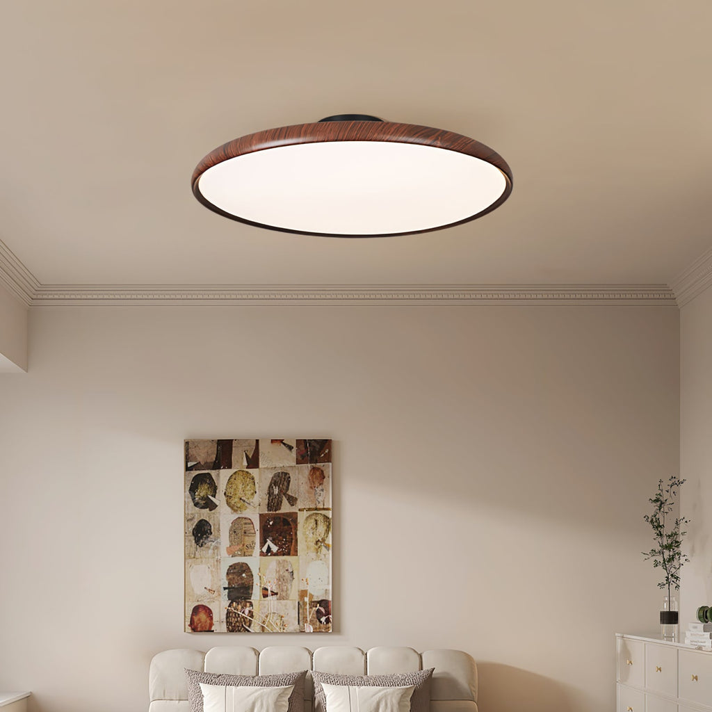 Walnut-grain Clérachic ceiling light with a white diffuser over a bed with a cream upholstered headboard and a framed collage.