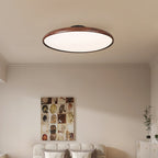 Walnut-grain Clérachic ceiling light with a white diffuser over a bed with a cream upholstered headboard and a framed collage.
