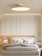 Light wood-grain Clérachic ceiling light seen from below, over a double bed with a pale quilt and warm wall panelling.