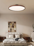 A walnut-grain Clérachic ceiling light above a bed with a tufted cream headboard and a collage artwork, in a calm bedroom.