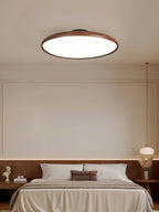 Walnut-grain Clérachic ceiling light above a bed with a dark wood headboard and a pendant lamp beside it.