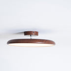 Low side view of this Clérachic ceiling light in walnut grain, with a matching round canopy and glowing diffuser.