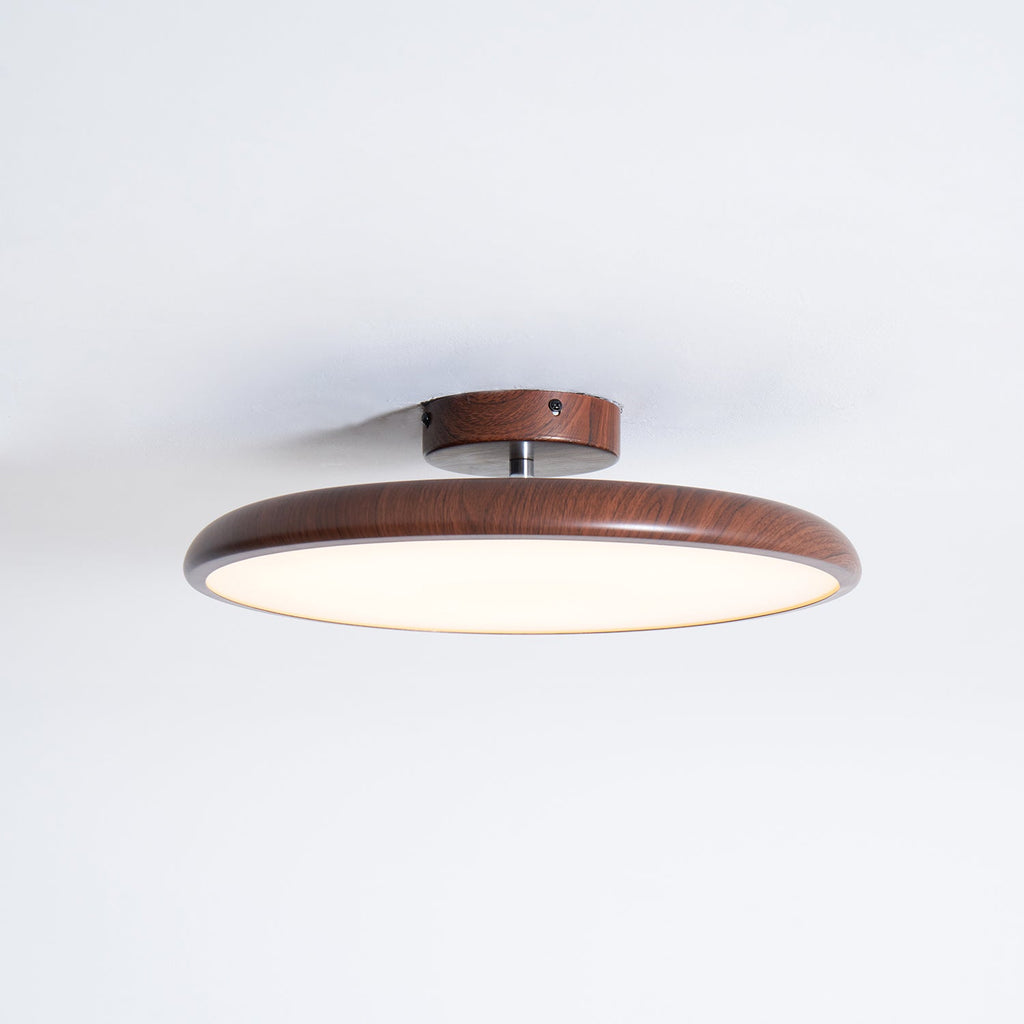 A walnut-grain Clérachic ceiling light in a slim flush profile, with the glowing diffuser visible from the side.