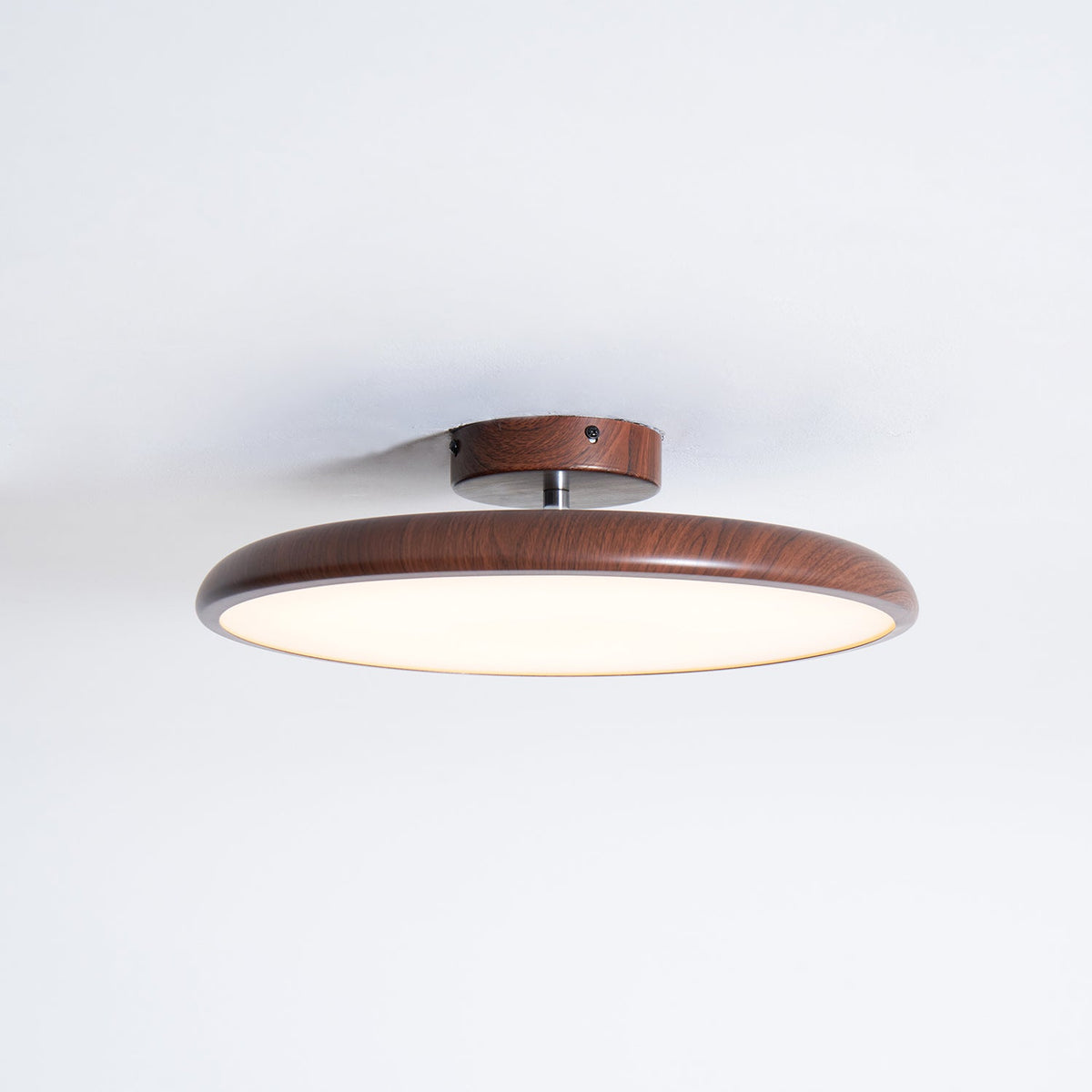 A walnut-grain Clérachic ceiling light in a slim flush profile, with the glowing diffuser visible from the side.