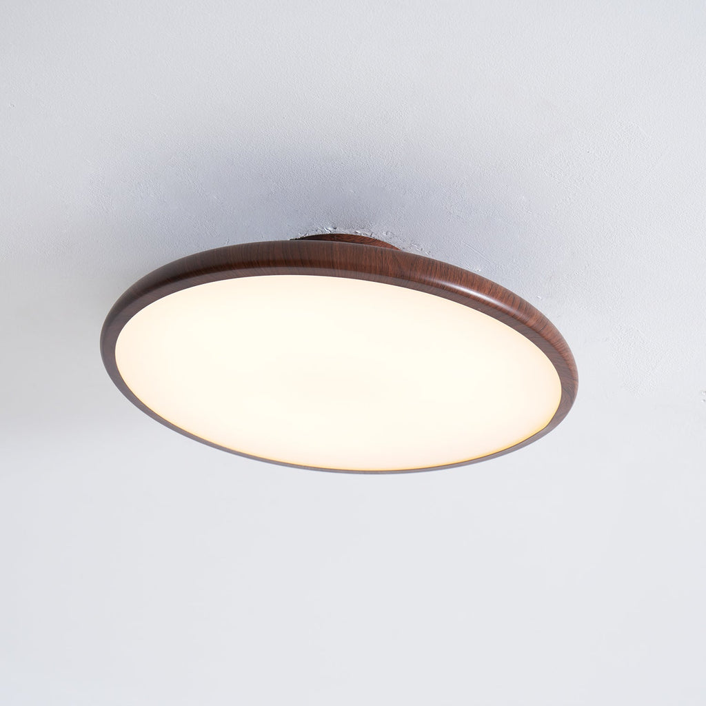 Underside of this Clérachic ceiling light in walnut grain, with its warm white diffuser filling the round frame.