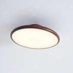 Underside of this Clérachic ceiling light in walnut grain, with its warm white diffuser filling the round frame.