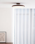 A walnut-grain Clérachic ceiling light above sheer white curtains and a framed line drawing of a figure.