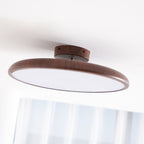 Angled view of this Clérachic ceiling light in walnut grain, with its white diffuser and a sheer curtain below.