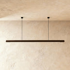 Clérachic's black walnut wood pendant bar hangs level from two thin cables against a plaster wall.