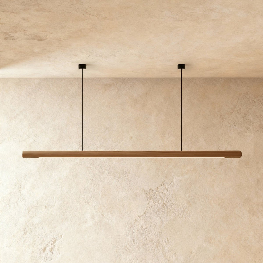 This Clérachic ash wood pendant bar glows softly along its length, hung from two thin ceiling cables.
