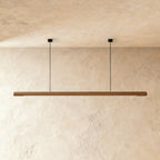 This Clérachic ash wood pendant bar glows softly along its length, hung from two thin ceiling cables.