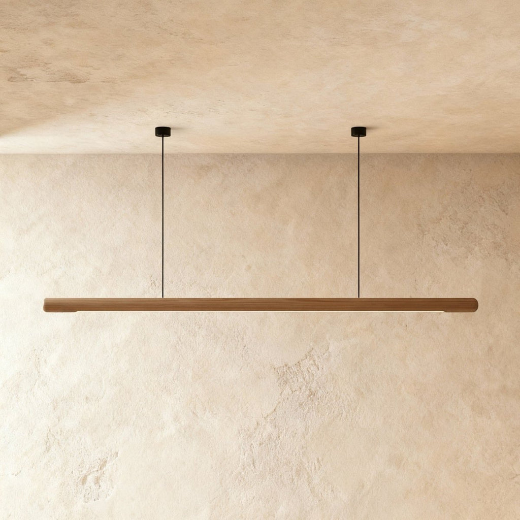 This Clérachic ash wood pendant bar spans the frame, its pale grain lit from below on a plaster wall.