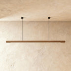 This Clérachic ash wood pendant bar spans the frame, its pale grain lit from below on a plaster wall.