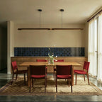 The long Clérachic black walnut pendant bar, joined by a brass band, lights a dining table with red chairs.