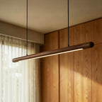 A Clérachic black walnut pendant bar glows in a wood-paneled dining room beside sheer curtains.