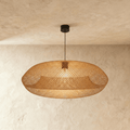 Clérachic woven rattan pendant light with a wide lozenge-shaped lattice shade, glowing warm against a plaster wall.