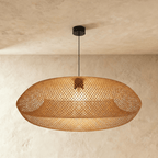 Clérachic woven rattan pendant light with a wide lattice shade glowing warm, viewed against a plaster ceiling.