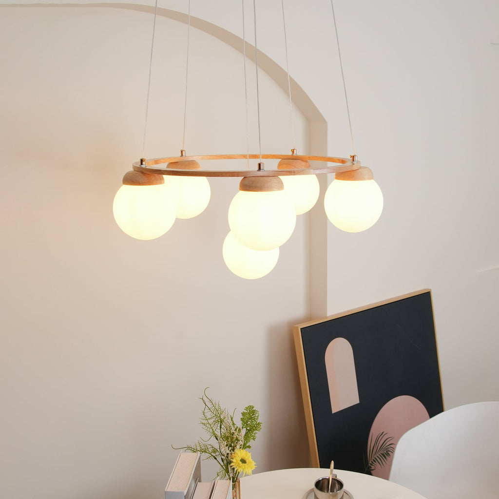 Lit, this Clérachic wood-ring chandelier hangs in front of an arched alcove, with a framed print and a small flower vase behind.