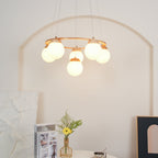 A Clérachic chandelier with frosted globes glowing under a wood ring, above a white table with flowers and magazines.
