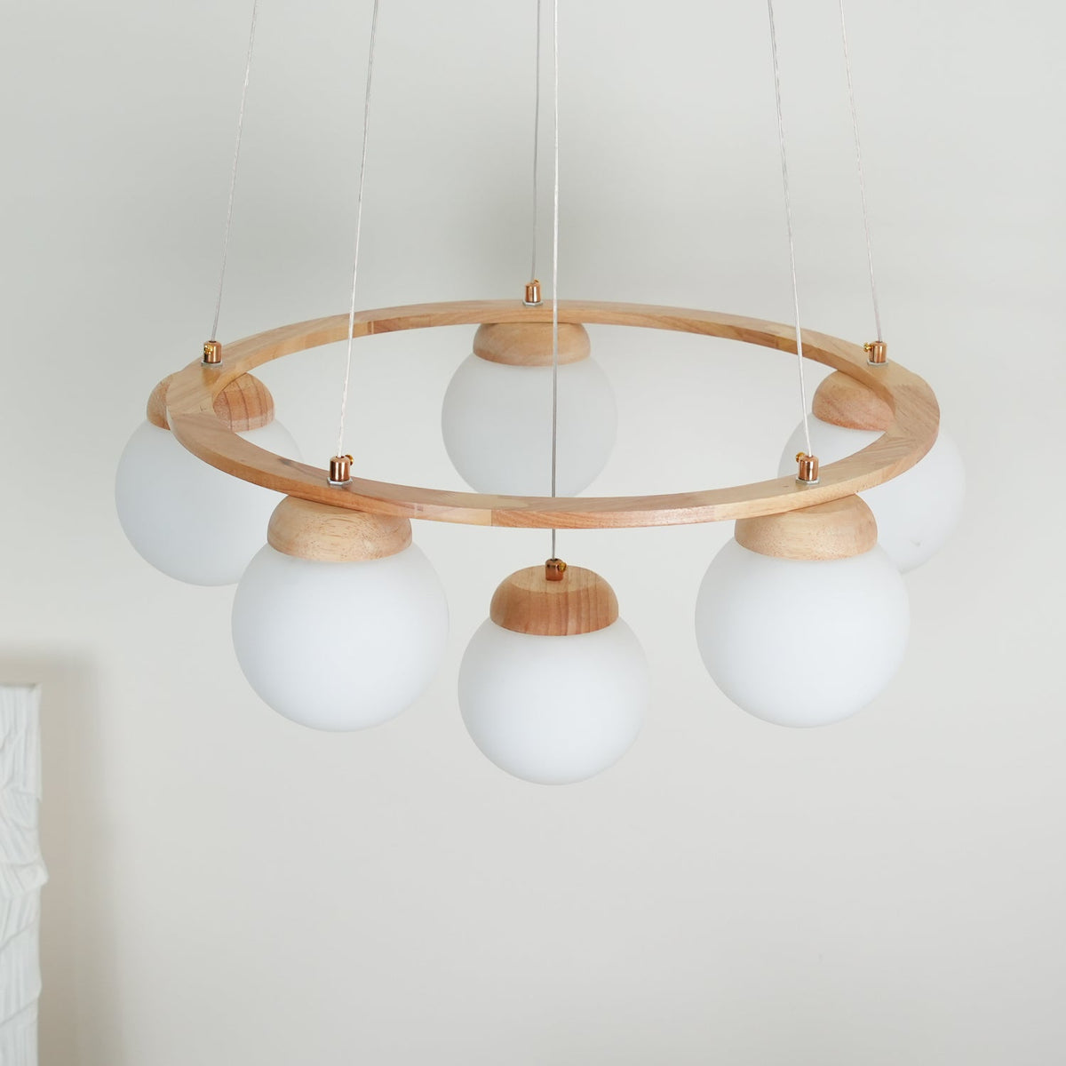 From a low angle, this unlit Clérachic chandelier shows its light wood ring, wire suspension and six frosted white globes.