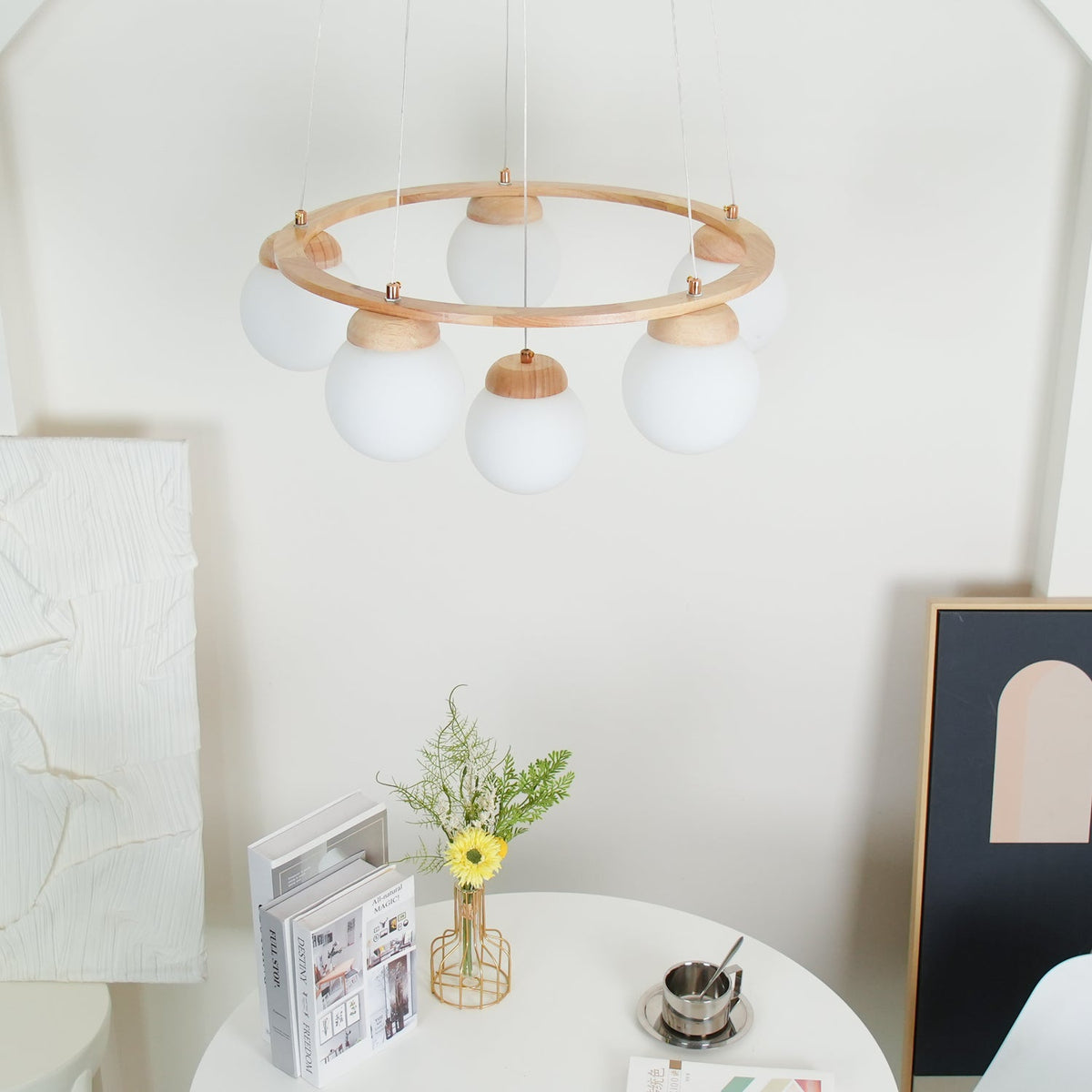 Unlit and seen from further back, this Clérachic wood-ring chandelier hangs above a white round table, a framed print and flowers.