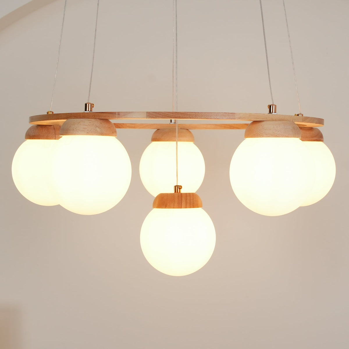 Side-on view of the warm-lit globes beneath the wood ring of this Clérachic chandelier, one globe hanging lower at the centre.