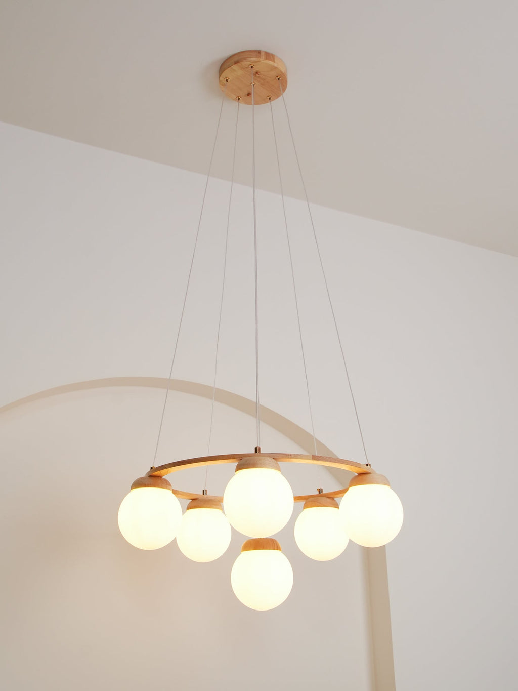 Hung from a wood ceiling plate on long wires, this lit Clérachic chandelier sits low in front of a white arched wall.