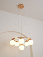 Hung from a wood ceiling plate on long wires, this lit Clérachic chandelier sits low in front of a white arched wall.