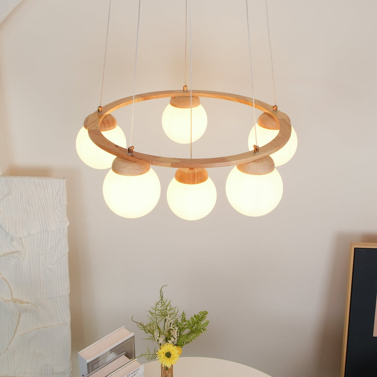 From below, the globes under the light wood ring of this Clérachic chandelier glow warm over a flower vase and books.