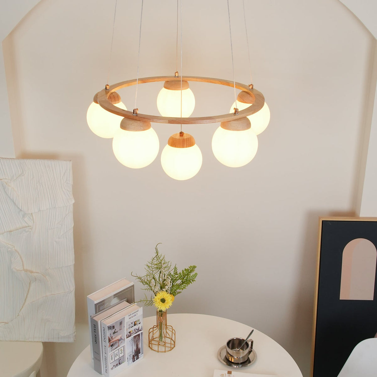 Soft glow from six frosted globes under a wood ring on this Clérachic chandelier, above a round white table with a framed print.