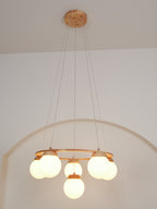 Full drop of this Clérachic chandelier from its round wood ceiling plate down to the lit globes, in front of a pale arch.
