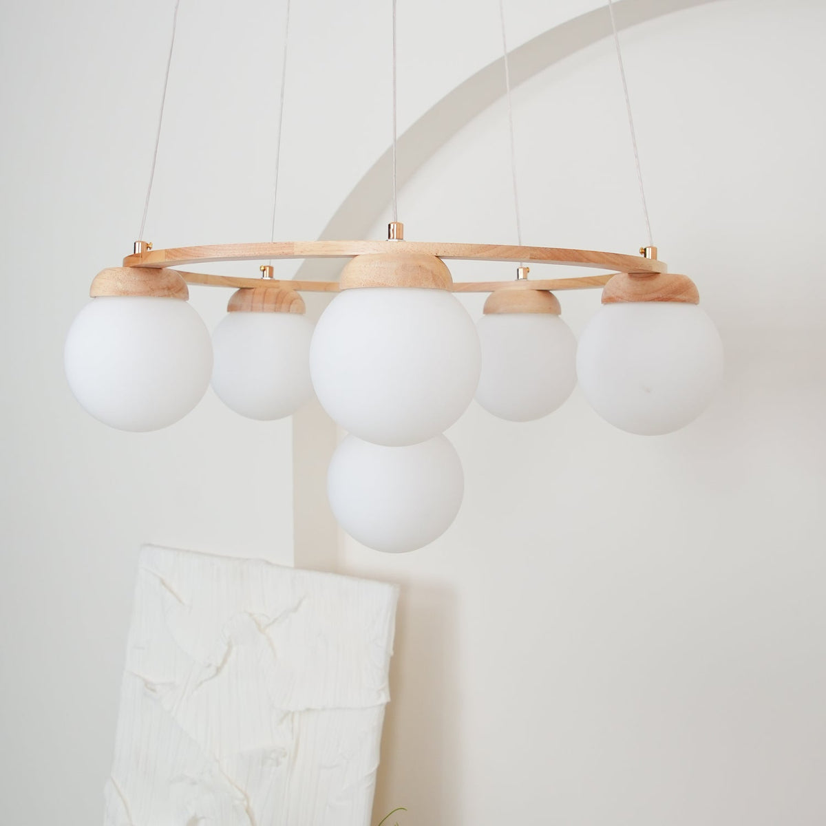 Unlit, the large frosted white globes and wood caps of this Clérachic chandelier hang below a thin ring, in front of a white arch.