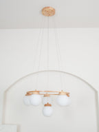 Hung from a wood ceiling plate against a white wall with an arch, this Clérachic chandelier shows five white globes.