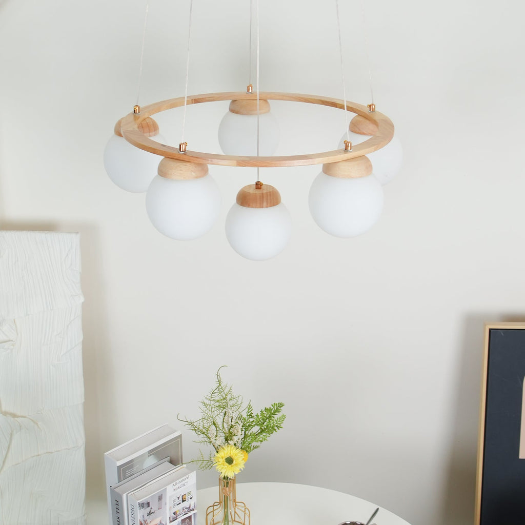 Looking up at this Clérachic wood-ring chandelier, with white globes under the ring and flowers and books on a table below.