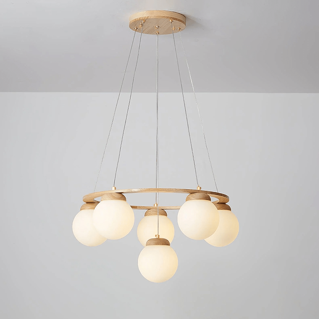 Warm light glows in the cream-tinted globes of this Clérachic chandelier, hung from a wood plate against a pale grey wall.